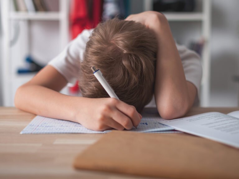Amélioration de la concentration via la sophrologie. Un adolescent fatigué et ennuyé fait ses devoirs sur un bureau dans sa chambre