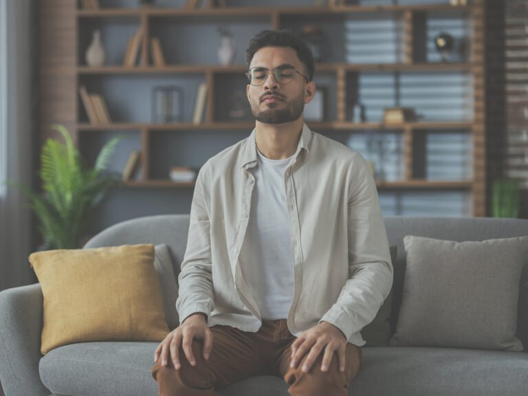 jeune homme effectuant un exercice de visualisation en sophrologie, assis sur un canapé.
